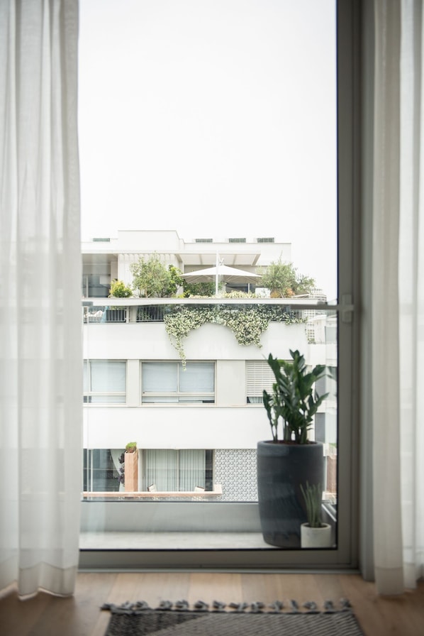 Un appartement moderne doté d’une grande fenêtre, d’une plante en pot et offrant une vue sur les immeubles voisins.