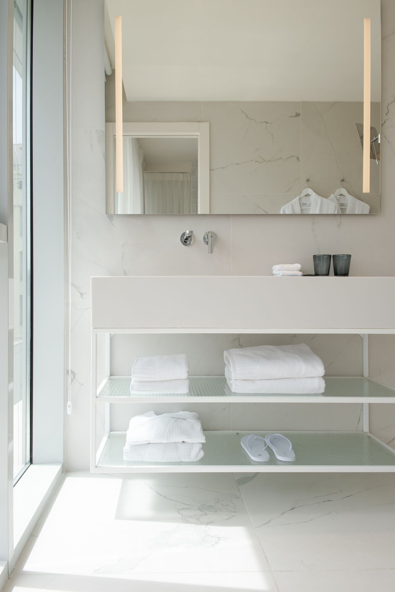 A modern bathroom with a large mirror, white marble tiles, and a glass shower enclosure.