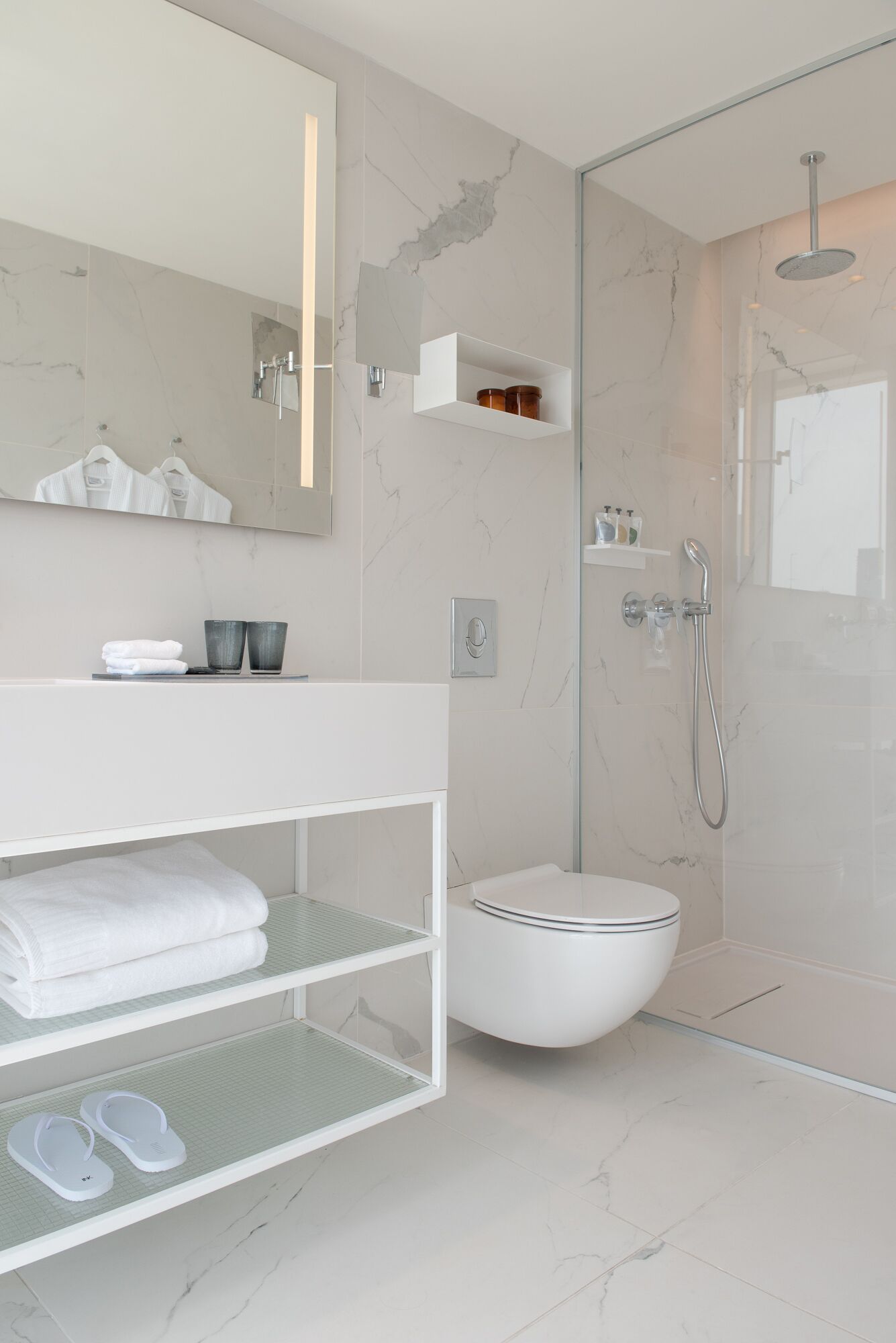 Un baño moderno con ducha de vidrio, tocador blanco con espejo y un inodoro.