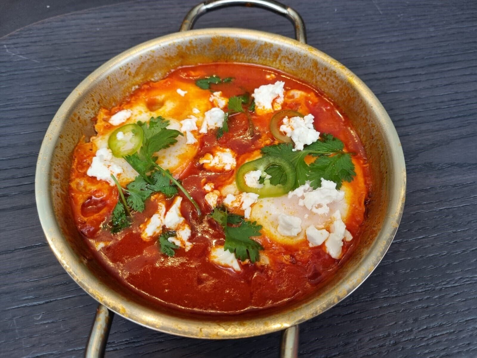 Eine Schüssel mit Essen, mit roter Soße, weißem Käse und grünen Jalapeños.