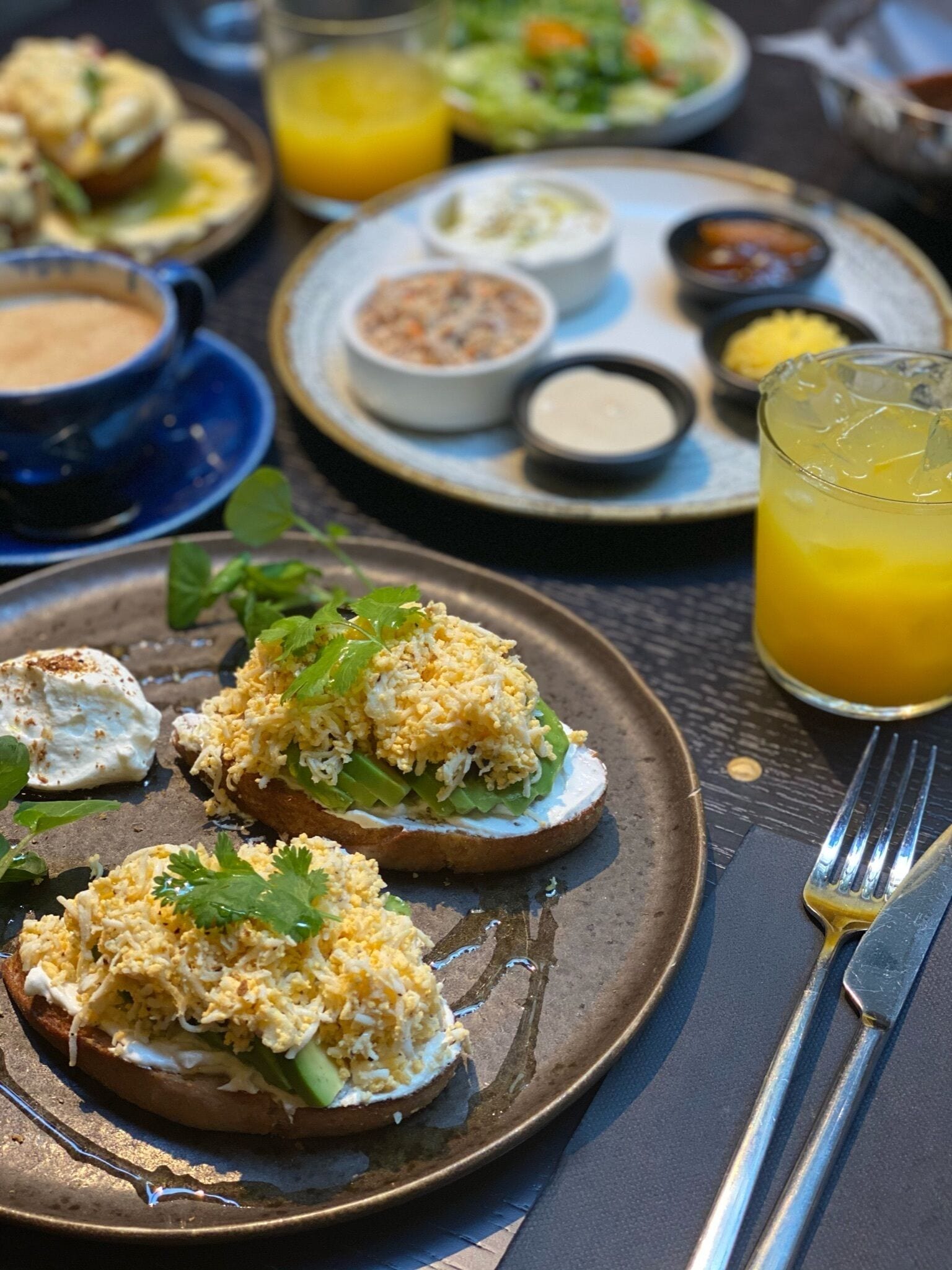 A dining table with plates of food, including toast with toppings, a glass of orange juice, and various side dishes.