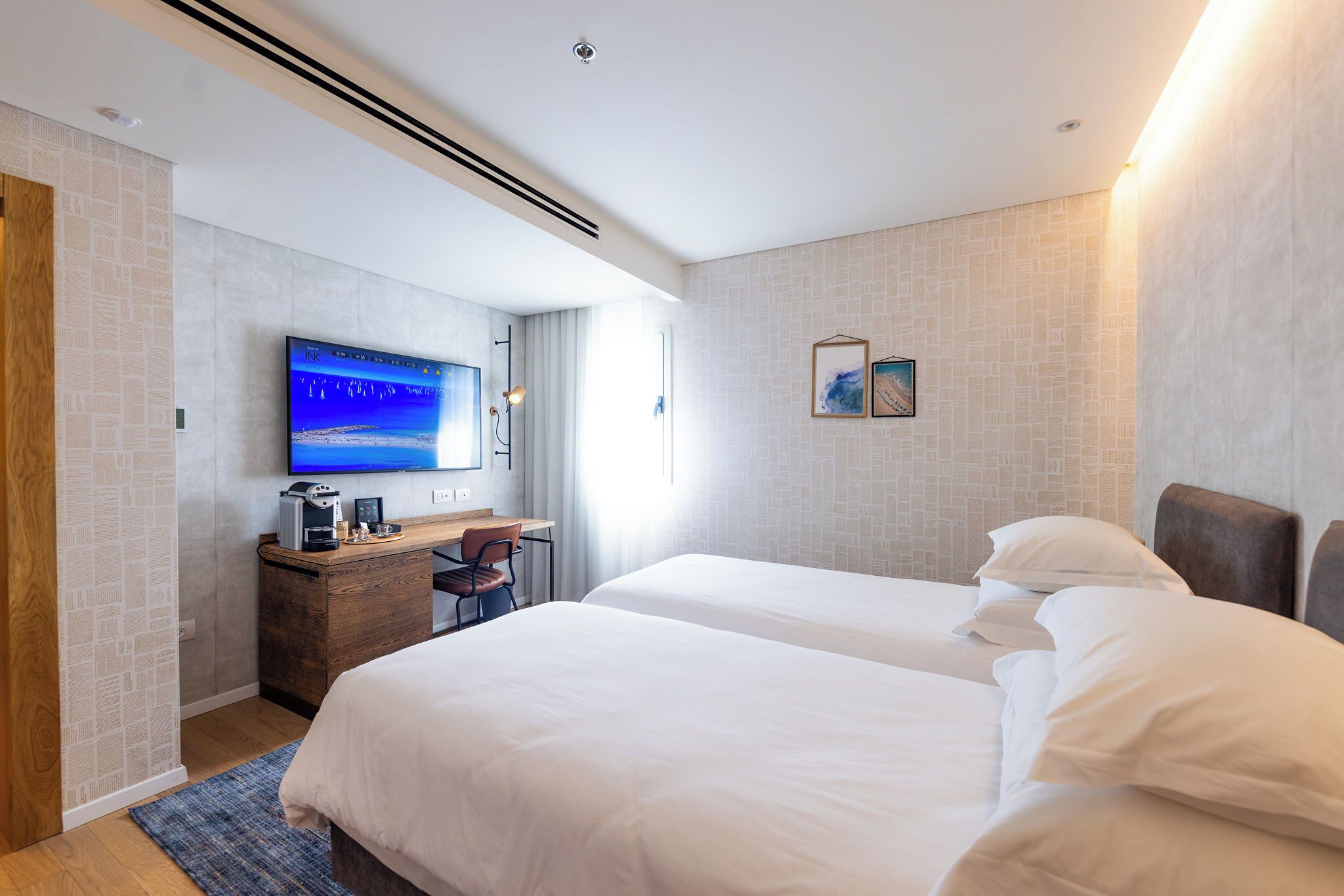A hotel room with two beds, a desk with a computer, a TV, and a coffee machine.