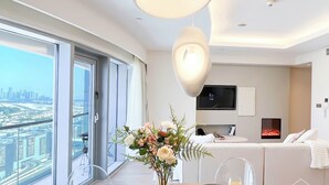Een moderne hotelkamer met een groot raam met uitzicht op de stad, een eetgedeelte met een tafel gedekt voor twee personen, en een gezellige zithoek met een open haard.