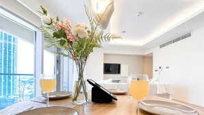 Een hotelkamer met een eettafel voor twee personen, een bloemenvaas en een balkon met uitzicht op de stad.