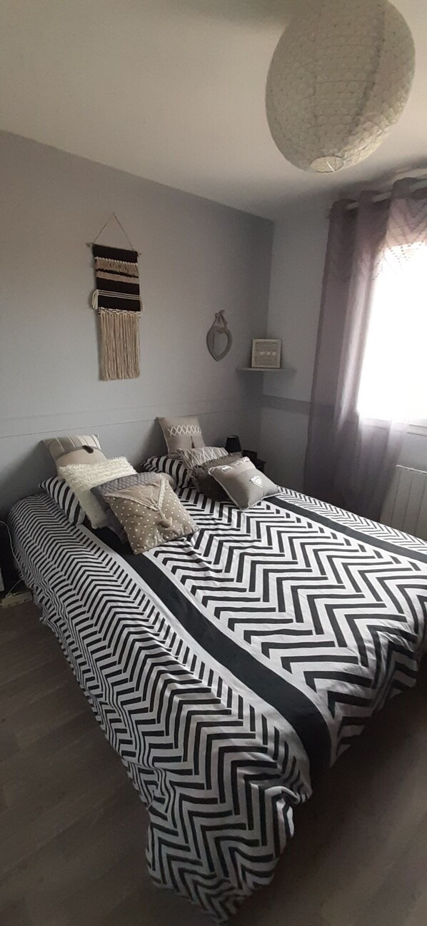 Une chambre à coucher avec un lit recouvert d’une couvre-lit à motifs zigzag noir et blanc, une décoration murale en macramé et un luminaire suspendu.