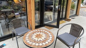 A glass-enclosed patio with wicker chairs and a mosaic table, reflecting a garden and outdoor furniture.