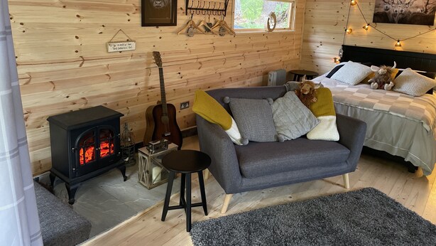 A cozy cabin interior with a wooden wall, a fireplace, a couch, a bed, and a guitar.