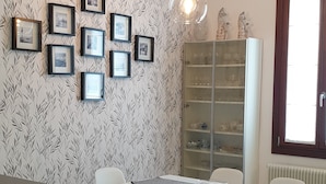 Ein Essbereich mit einem weißen Tisch und Stühlen, gerahmten Bildern an der Wand, einer Uhr und einem Schrank mit Glastüren.