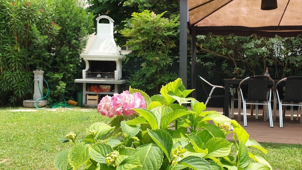 Ein Patio-Bereich mit Grill, Gartenmöbeln und üppiger Bepflanzung.
