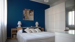 Ein Schlafzimmer mit einem Bett, Nachttischlampen, einem Bücherregal und einem Gemälde an der Wand.