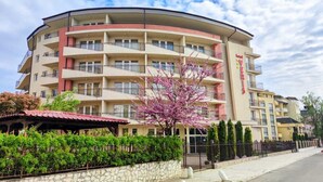 Un hotel de varios pisos con balcones, un muro de piedra y un cerezo en flor.