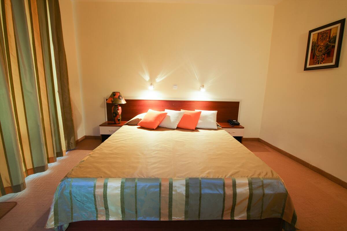 Una habitación de hotel con una cama grande, una mesita de noche con lámpara y un cuadro en la pared.