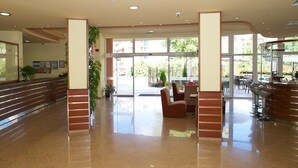 Un vestíbulo amplio con piso pulido, una recepción y una zona de estar con vista al exterior.