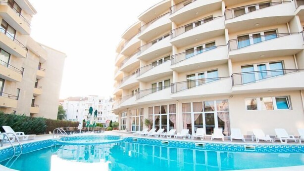 Una piscina rodeada de sillas de descanso blancas y un edificio con balcones.