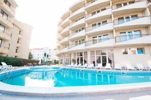 A swimming pool surrounded by white lounge chairs and a building with balconies.
