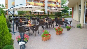 Un patio al aire libre con mesas, sillas, sombrillas y plantas en macetas.