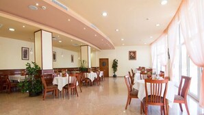 Un comedor amplio con varias mesas y sillas, piso pulido y ventanas grandes que dejan entrar luz natural.