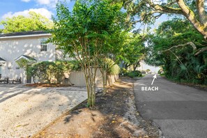 Eine Wohnstraße mit einem Haus, einem Baum und einem Gehweg, der zum Strand führt.