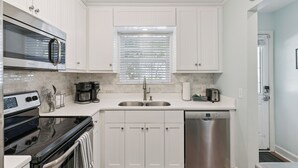 Una cocina moderna con armarios blancos, electrodomésticos de acero inoxidable y una ventana con persianas.