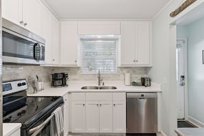 Una cocina moderna con armarios blancos, electrodomésticos de acero inoxidable y una ventana con persianas.