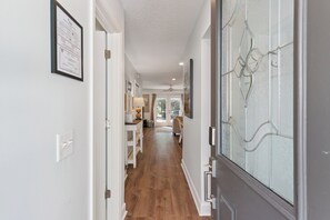 A hallway with a door on the right, a framed certificate on the left, and a dining area in the background.