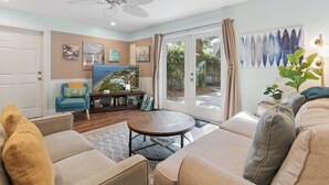 Sala de estar con ventilador de techo, televisor y vista a un patio trasero con piscina.