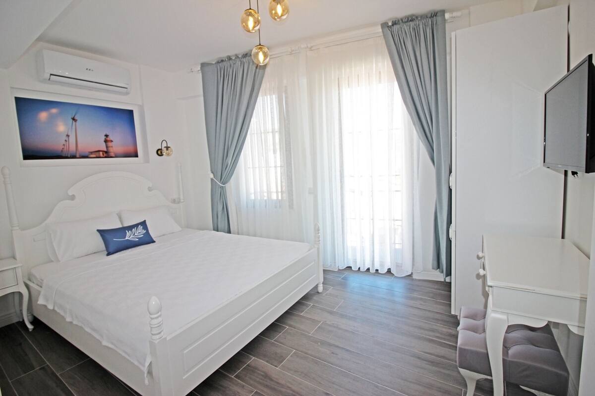A bedroom with a large bed, a desk, a TV, and a painting of a lighthouse.