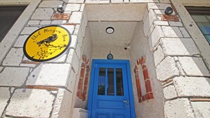 A building with a blue door and a yellow sign with a bird and text. - Otel Meryem Ana Bozcaada (Bozcaada)
