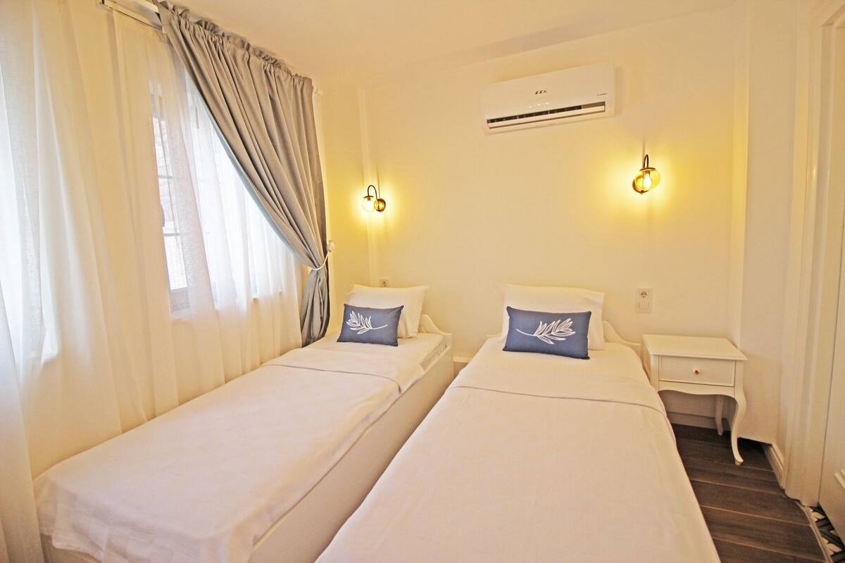 A hotel room with two single beds, a nightstand, an air conditioning unit, and two wall-mounted lights.