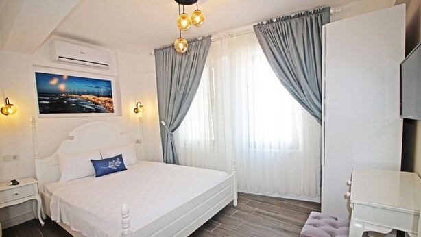 A bedroom with a bed, bedside tables, a desk, and a chair. - Otel Meryem Ana Bozcaada (Bozcaada)