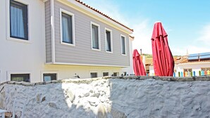 A two-story building with a stone wall in front. - Otel Meryem Ana Bozcaada (Bozcaada)