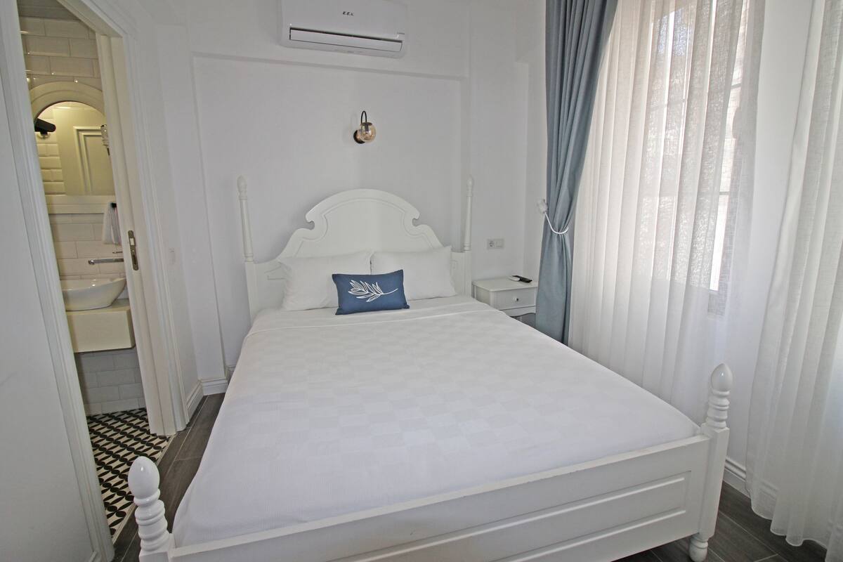 A white four-poster bed with a blue pillow, a bedside table, and a nightstand.