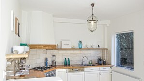 A modern kitchen with white cabinets, a wooden countertop, a gas stove, and a hanging light fixture.