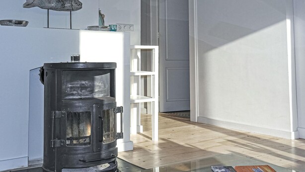A modern living room with a wood-burning stove, a white shelving unit, and a glass coffee table.