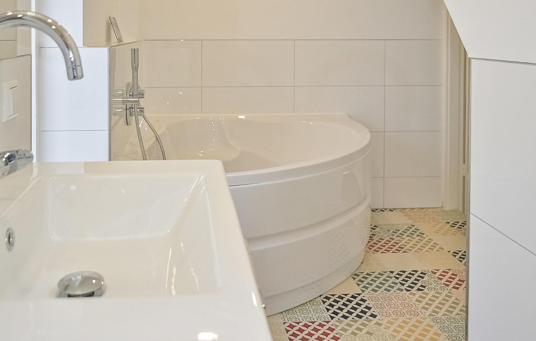 Un baño con una bañera blanca, un lavabo blanco y una ducha. El suelo presenta un diseño de baldosas estampado.
