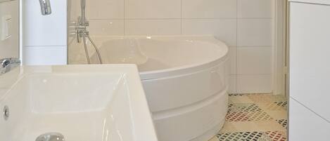 Un baño con una bañera blanca, un lavabo blanco y una ducha. El suelo presenta un diseño de baldosas estampado.
