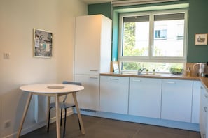 A modern kitchen with white cabinets, a round table, and a window with a view of greenery outside.