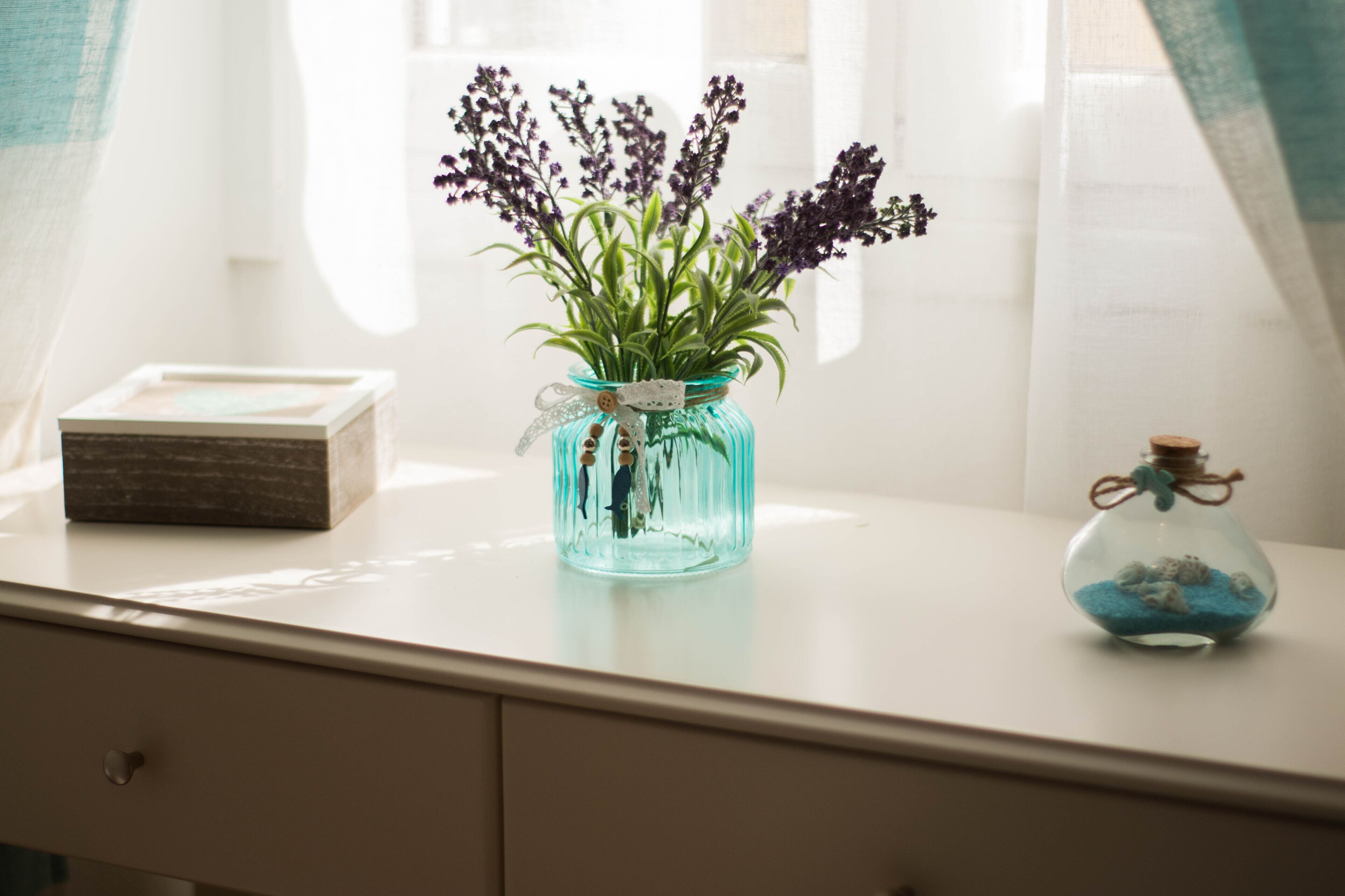 Vista clara de una habitación con un escritorio blanco, un jarrón con flores y un pequeño adorno de vidrio.