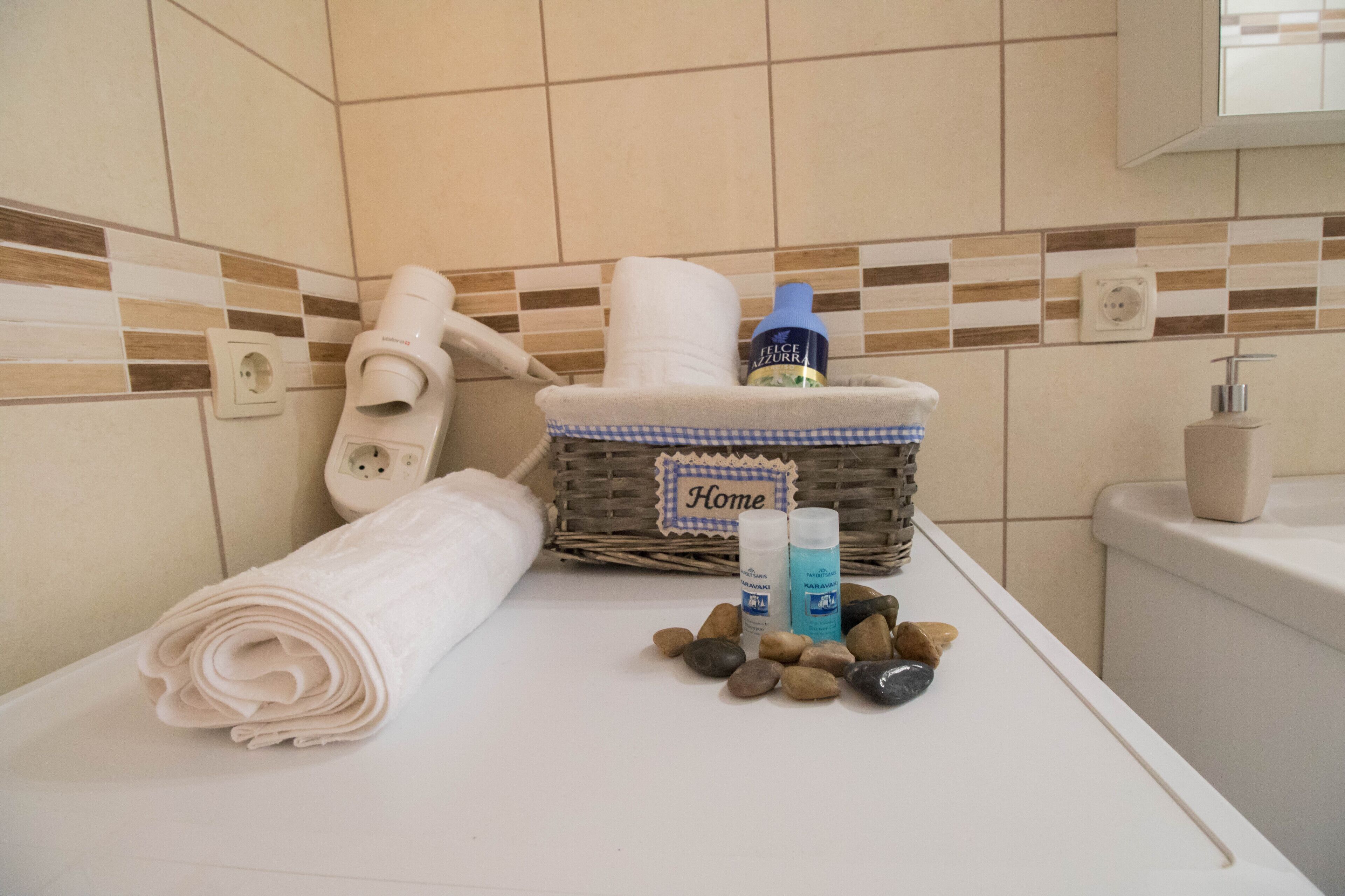 A bathroom with a white towel, a wicker basket labeled "Home," and toiletries on the counter.