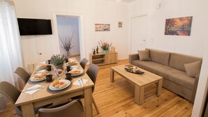 Un coin repas avec une table en bois, des chaises et un canapé. Un téléviseur est fixé au mur, et un tableau est accroché au mur.