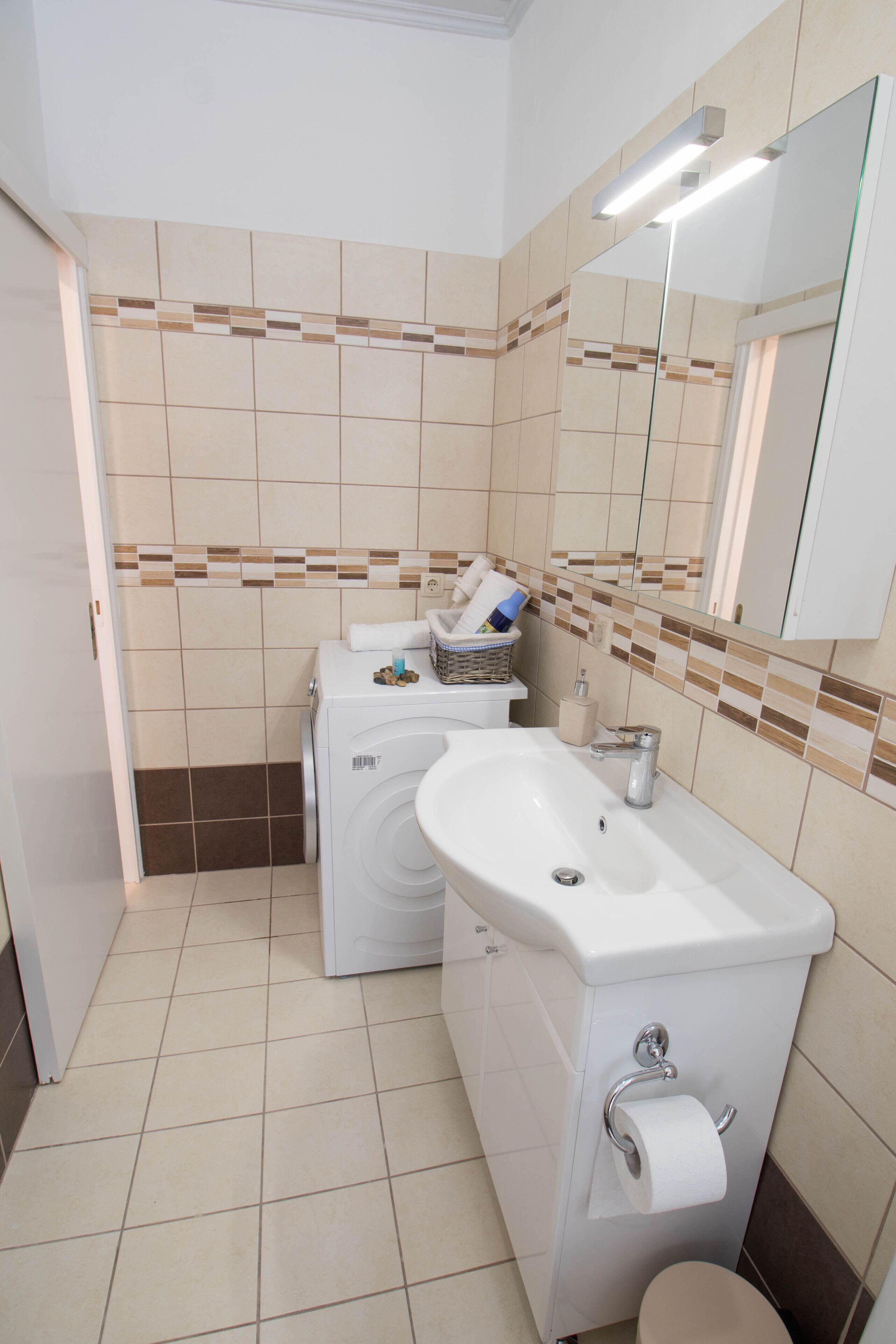 Une salle de bain avec un lavabo blanc, un miroir, des toilettes et un lave-linge.
