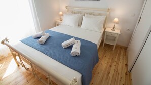 Un lit bien fait, avec des draps blancs et une couverture bleue, deux lampes de chevet et un tableau au mur.