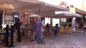 Un café en plein air avec des tables et des chaises sous des parasols, un panneau affichant le menu et un distributeur automatique de billets.