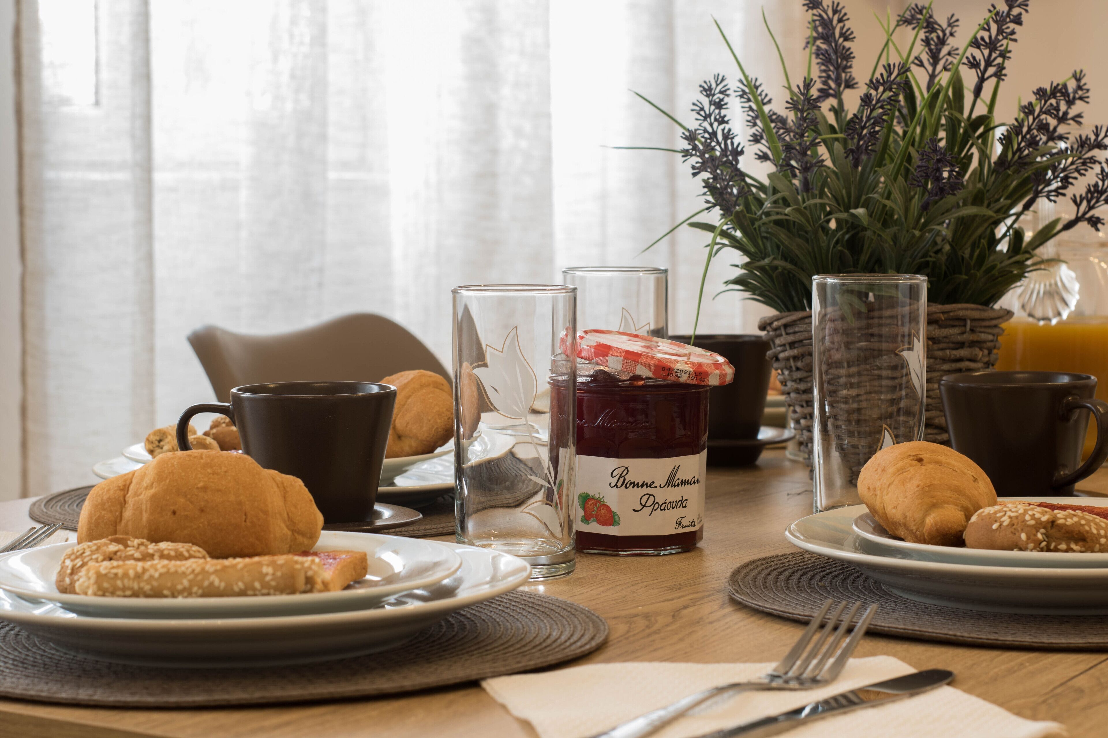 A breakfast setting with croissants, a glass of jam, and a coffee cup on a wooden table.