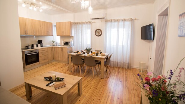 Une cuisine moderne avec des meubles en bois, un coin repas avec une table et des chaises, et un téléviseur fixé au mur.