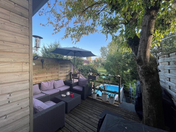 Una terraza de madera con mobiliario exterior, una piscina y un árbol.