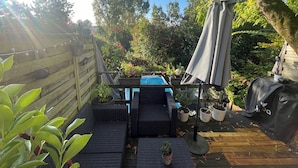 Een houten terras met tuinmeubilair, een barbecue en potplanten.