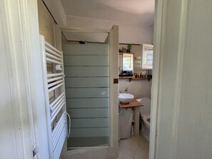 Un pasillo estrecho que conduce a un baño con ducha, lavamanos e inodoro.