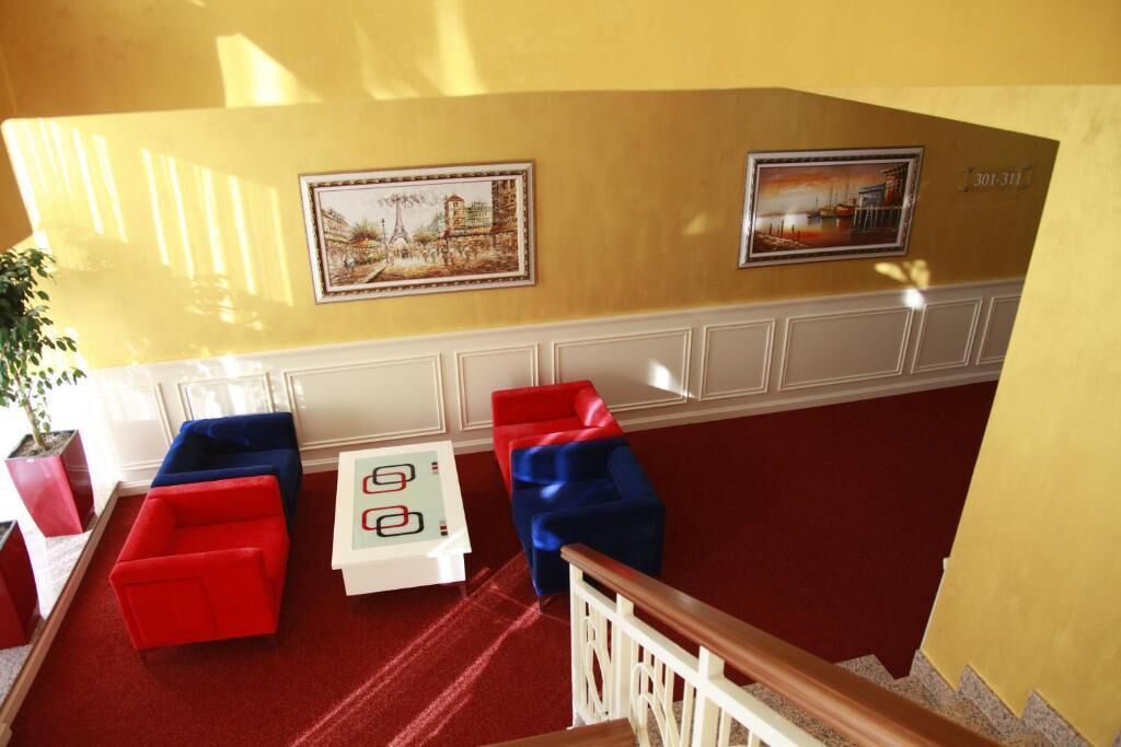 A lobby with red and blue chairs, a small table, and two framed pictures on the wall.
