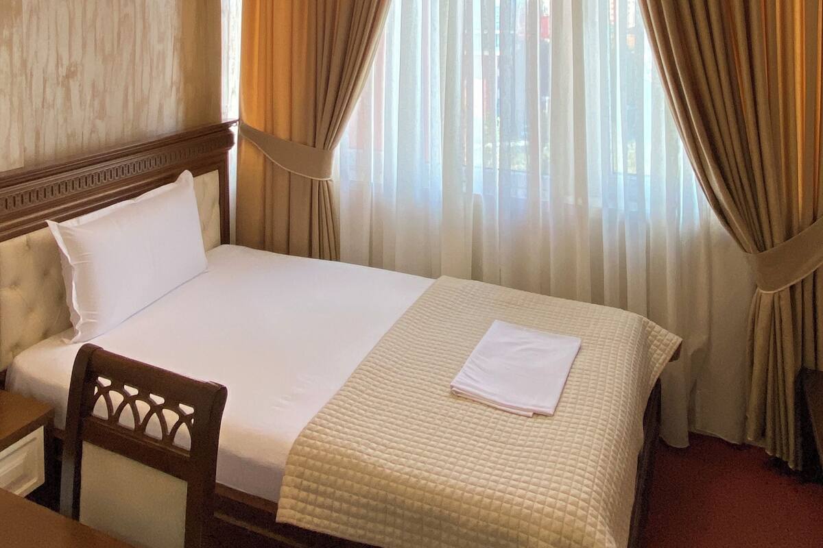 Ein Hotelzimmer mit einem Bett, einem Holz-Kopfteil, einem Nachttisch, einem Sessel und einem großen Fenster mit Vorhängen.